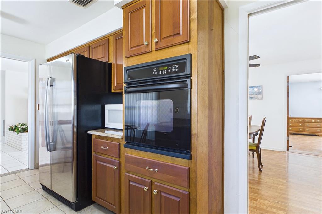 Kitchen with black oven, freestanding refrigerator, wood finish cabinets, and white microwave
