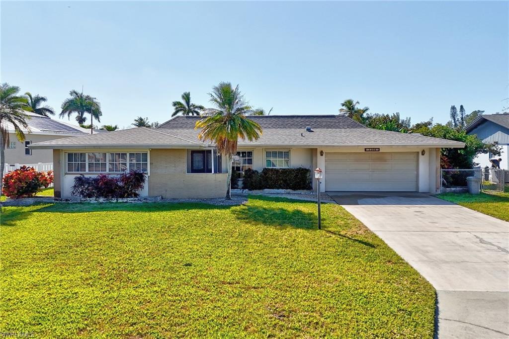 Ranch-style house featuring a front yard, an attached garage, concrete driveway, roof with shingles, and brick siding