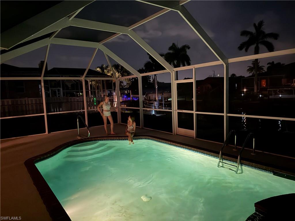 Screened pool area featuring an illuminated pool with integrated steps and a metal ladder