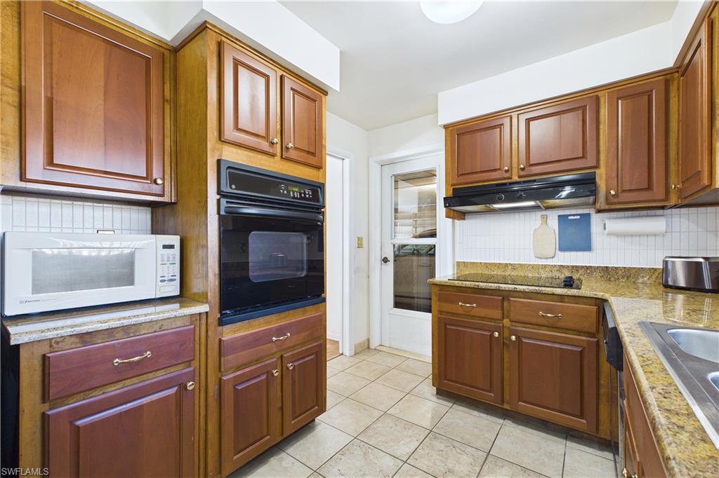 Kitchen featuring black oven, white microwave, backsplash, light tile patterned flooring, and light stone countertops