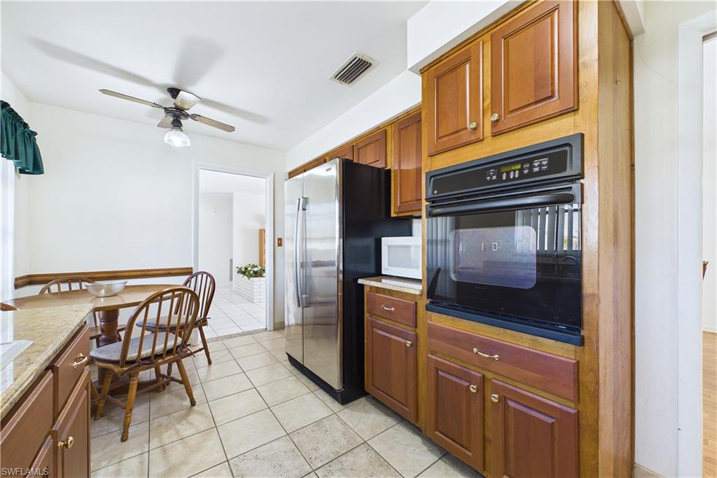 Kitchen featuring oven, white microwave, light tile patterned floors, freestanding refrigerator, and a ceiling fan