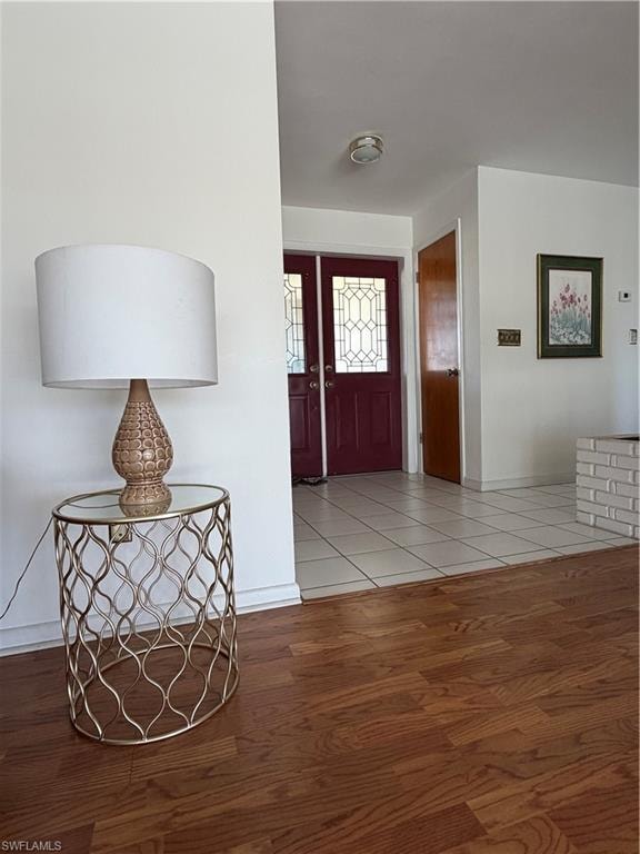 Entryway featuring a double door with decorative glass inserts, ceramic tile flooring, and a contrasting wood-finish floor in the adjacent area