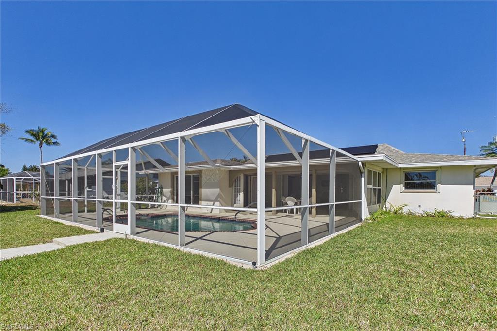 Back of property with a lawn, stucco siding, a sunroom, a lanai, and an outdoor pool