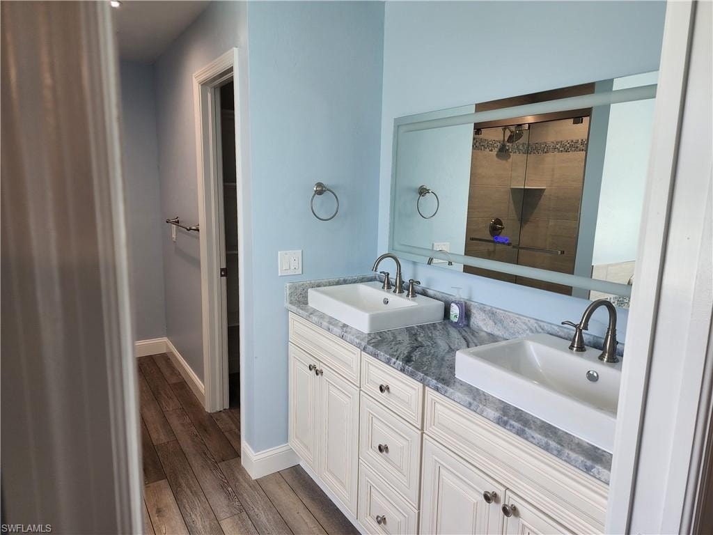 Full bathroom featuring double vanity, a tile shower, and yinyl wood-style flooring