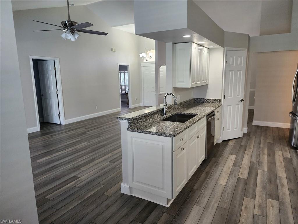 Kitchen with white cabinetry, medium stone counters, vinyl wood-type flooring, ceiling fan, and vaulted ceiling