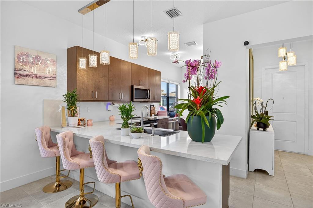 Kitchen with a peninsula, hanging light fixtures, a kitchen breakfast bar, light stone countertops, and light tile patterned floors