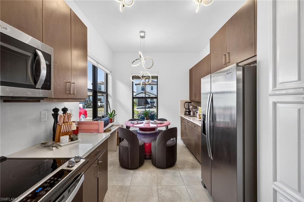 Kitchen with stainless steel appliances, hanging lights, light stone countertops, and light tile patterned floors