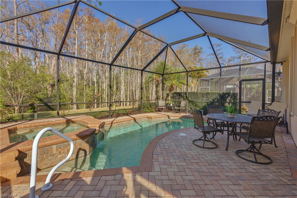 Relaxing pool / spa featuring glass enclosure, a patio area, outdoor dining area, and a sunroom