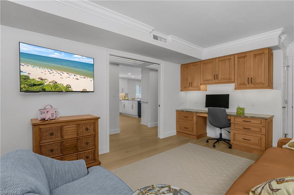 3rd bedroom currently used as an office area, with built in study area, light wood floors, and ornamental molding, leather pull out sofa, new hurricane window and a closet.