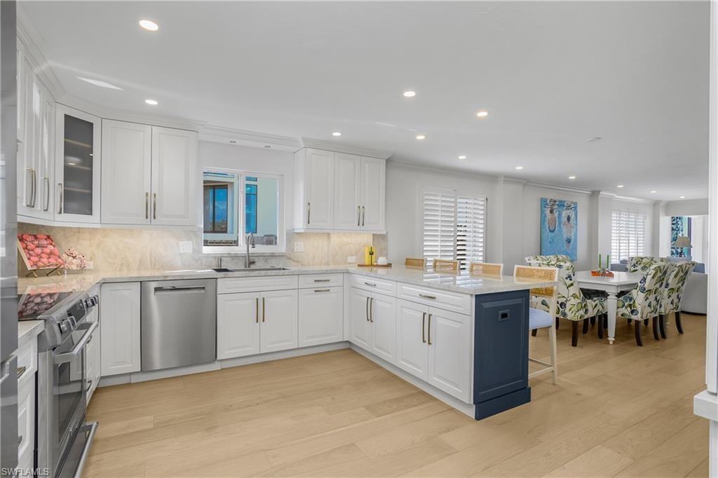 Kitchen featuring a kitchen bar, a peninsula, stainless steel appliances, light wood flooring, and white cabinetry, with storage pantry and coffee bar cabinetry