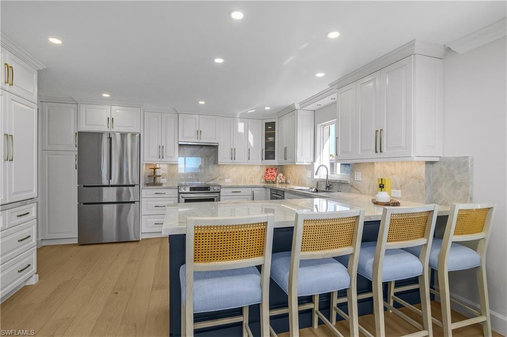 Custom kitchen featuring stainless steel appliances, a breakfast bar, light stone countertops, light wood  flooring, and dual tone cabinetry, pantry and coffee bar cabinetry.
