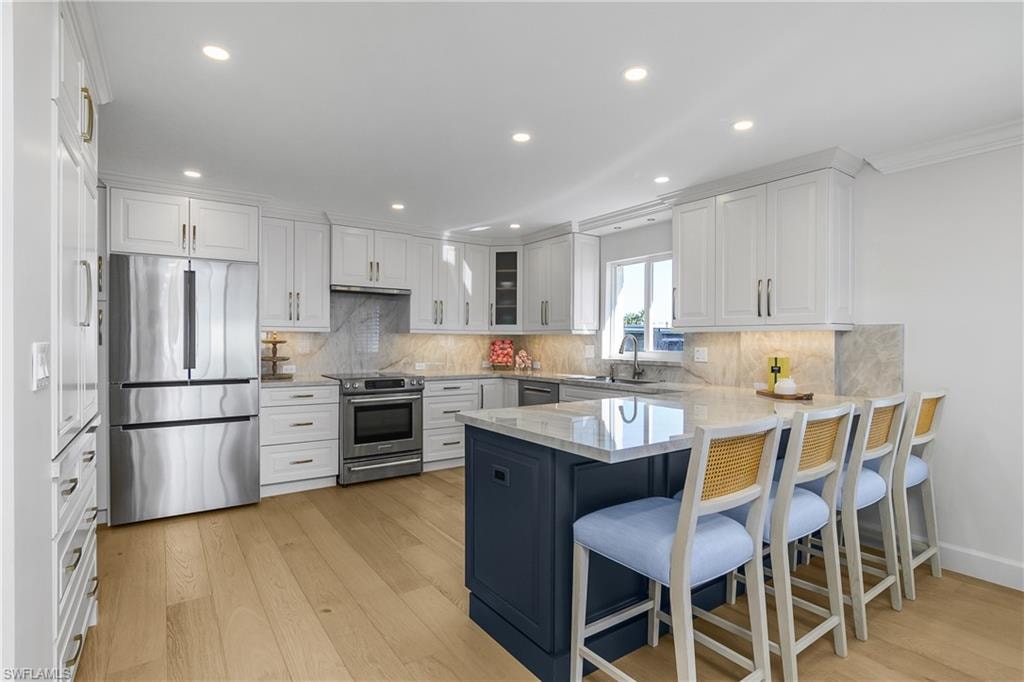 Kitchen with stainless steel appliances, a breakfast bar area, light stone countertops, dual tone cabinetry, and light wood-style floors