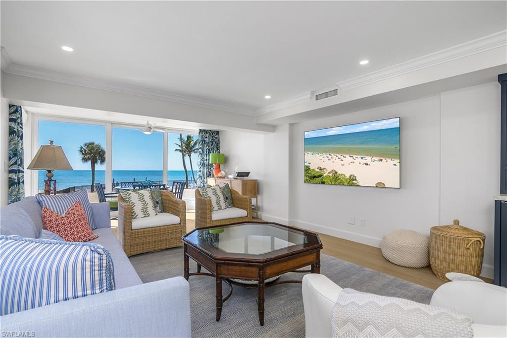 Living area featuring custom wood flooring, a water view, crown molding, and recessed lighting