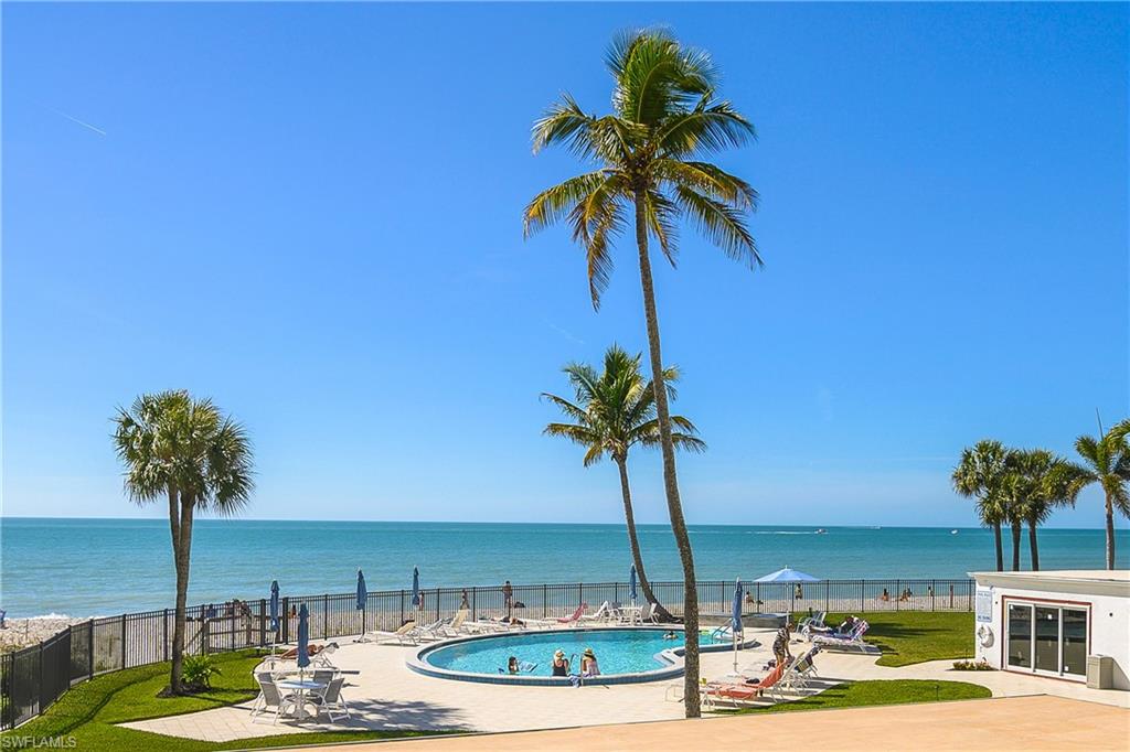 Embassy Club pool featuring a relaxing patio area, gated beach access, a water view, and a fenced backyard