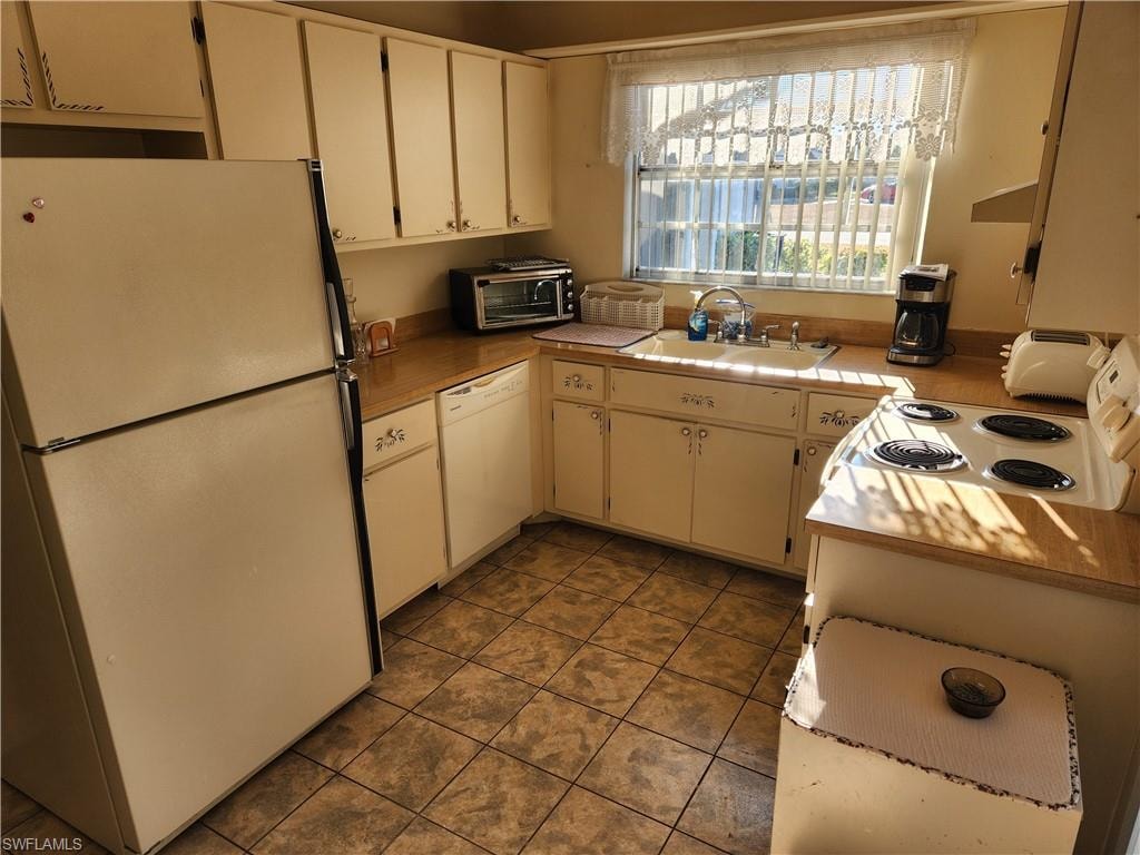 Kitchen featuring white appliances, light countertops, white cabinetry, and dark tile patterned floors
