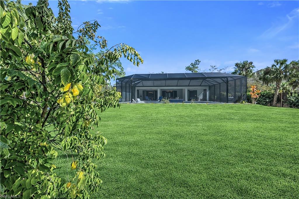 Back of property with glass enclosure, a sunroom, a lawn, and an outdoor pool