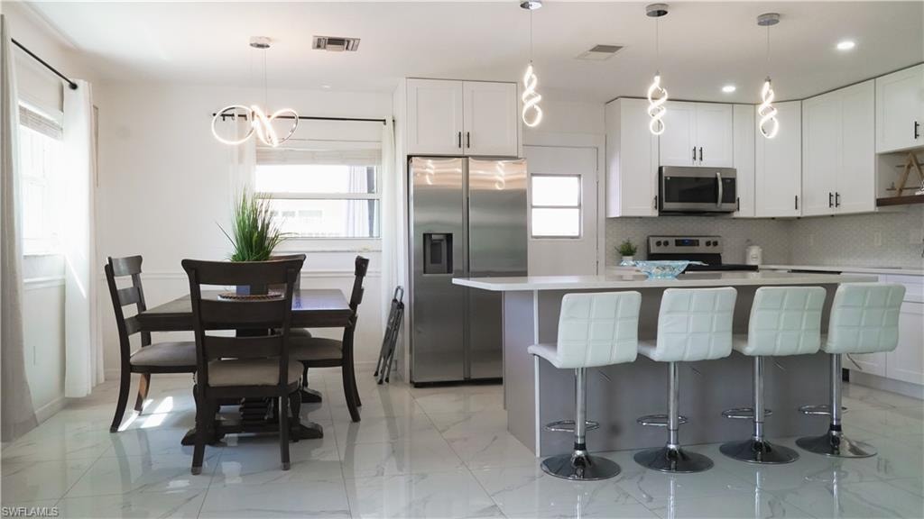 Kitchen featuring stainless steel appliances, a kitchen breakfast bar, a kitchen island, two tone cabinetry, and tasteful backsplash