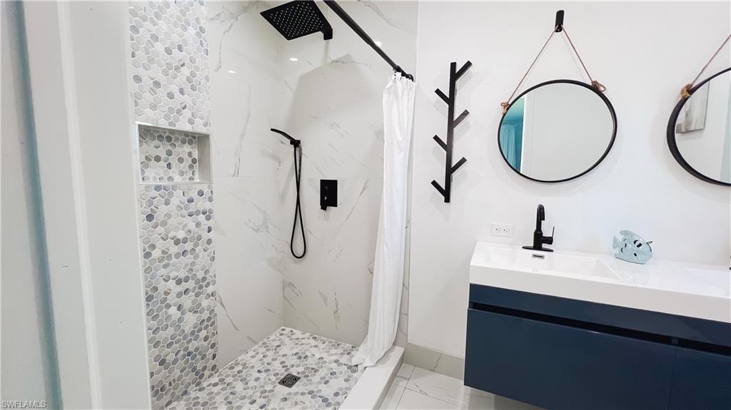 Bathroom with a marble finish shower, vanity, and light marble finish floors