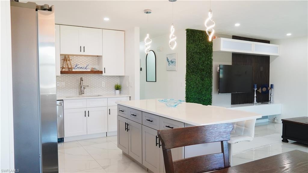 Kitchen with freestanding refrigerator, hanging light fixtures, open shelves, backsplash, and light stone counters