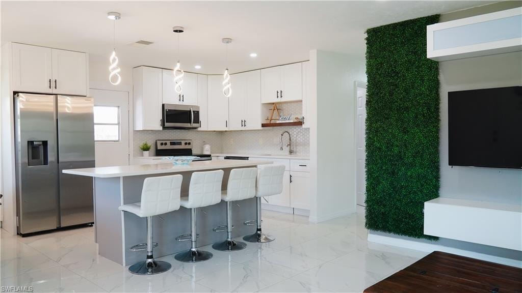 Two tone kitchen with stainless steel appliances, pendant lighting, a kitchen island, a breakfast bar area, and open shelves