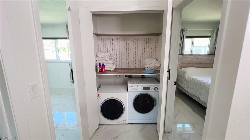 Laundry area with light marble finish floors, plenty of natural light, and washing machine and dryer