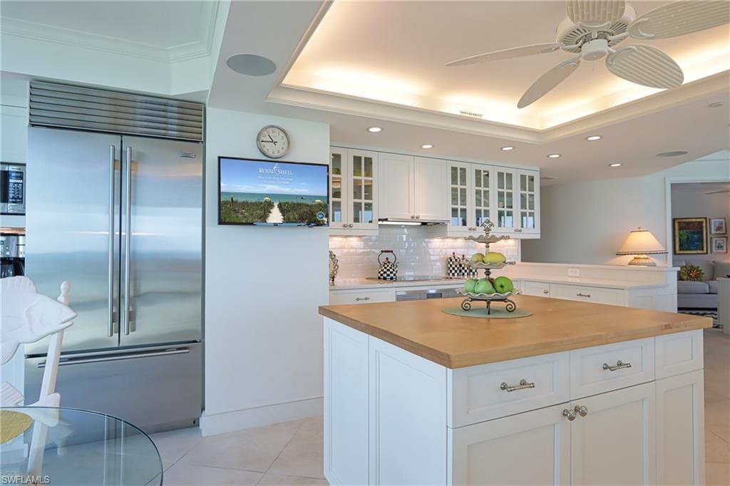 Kitchen featuring ceiling fan, butcher block counters, built in appliances, glass fronted cabinets, and white cabinets