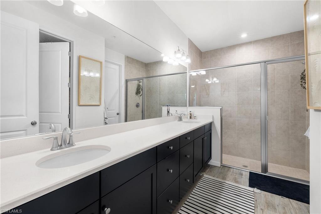 Full bathroom with double vanity, a stall shower, and light wood finished floors