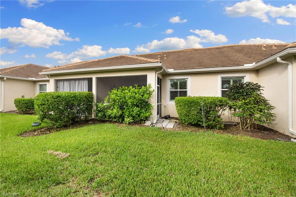Rear view of house with stucco siding, a lawn, and a tile roof