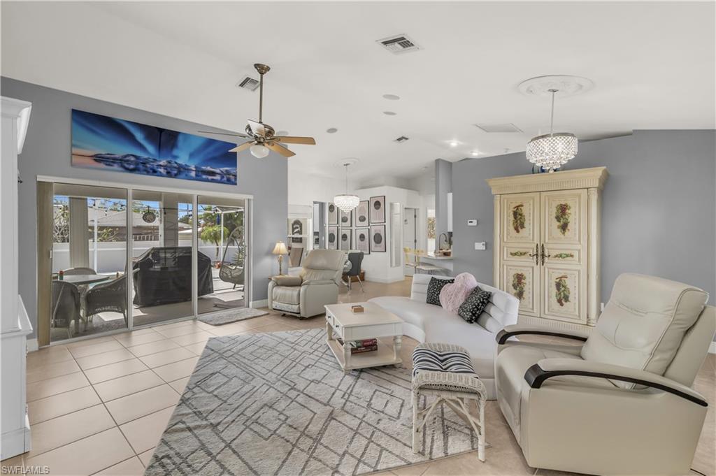 Living area featuring vaulted ceiling, light tile patterned floors, a ceiling fan, and a chandelier