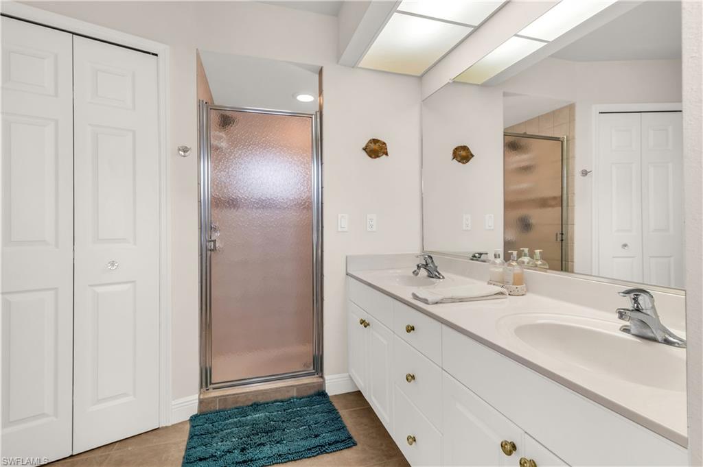 Bathroom with a closet, a stall shower, double vanity, and light tile patterned floors