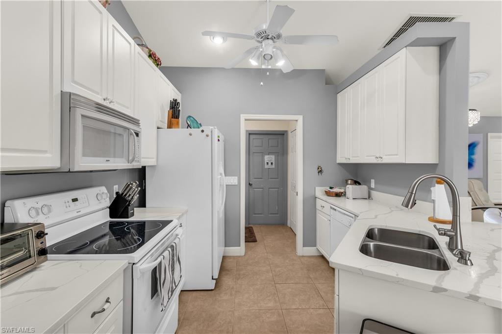 Kitchen featuring white appliances, white cabinets, light stone countertops, ceiling fan, and light tile patterned floors