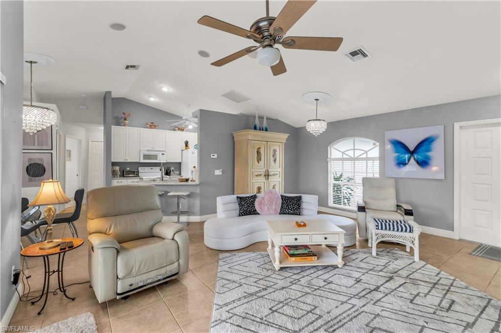 Living room with hanging lights, light tile patterned floors, vaulted ceiling, and a ceiling fan