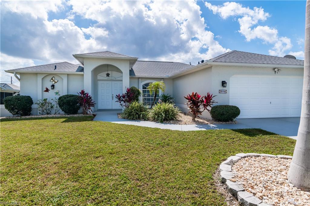 Ranch-style home with stucco siding, roof with shingles, a front yard, and a garage