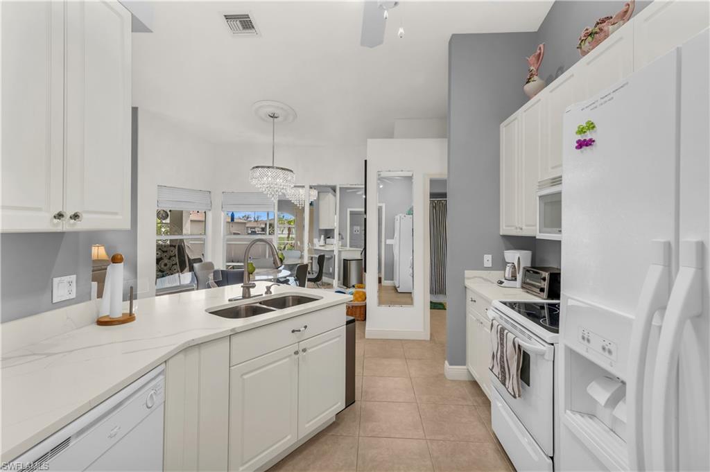 Kitchen featuring white appliances, hanging lights, white cabinetry, light stone countertops, and a peninsula