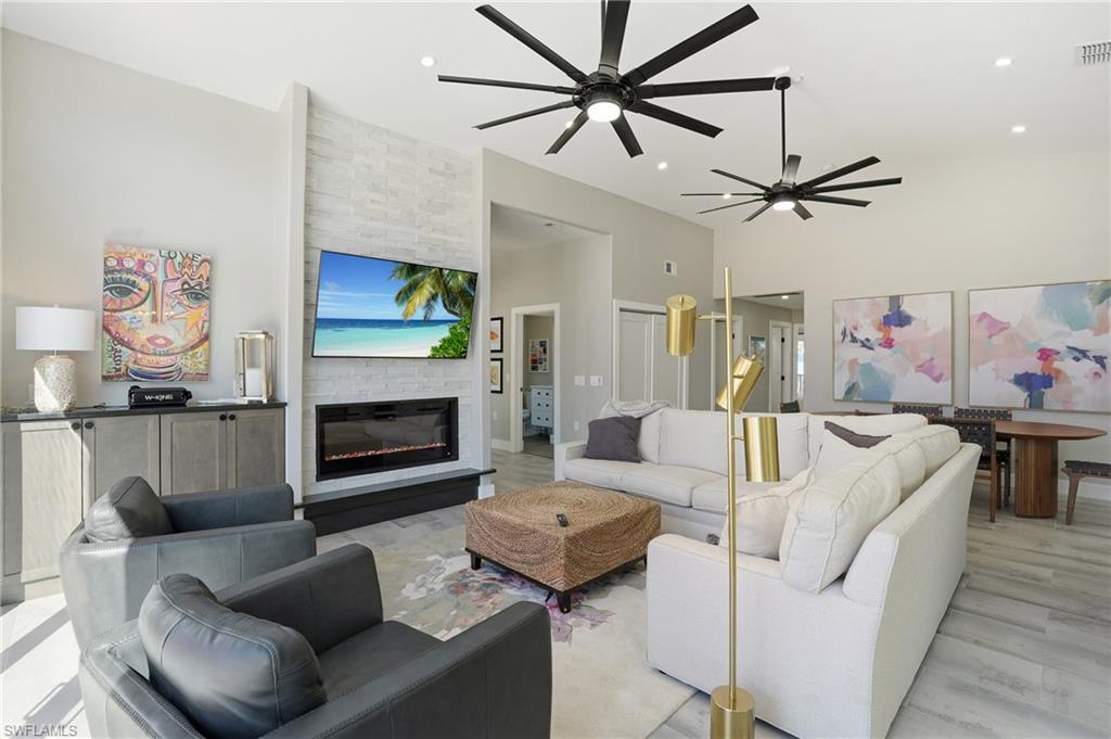 Living room featuring a large fireplace, ceiling fan, vaulted ceiling, and wood finished floors - Virtually Edited Image
