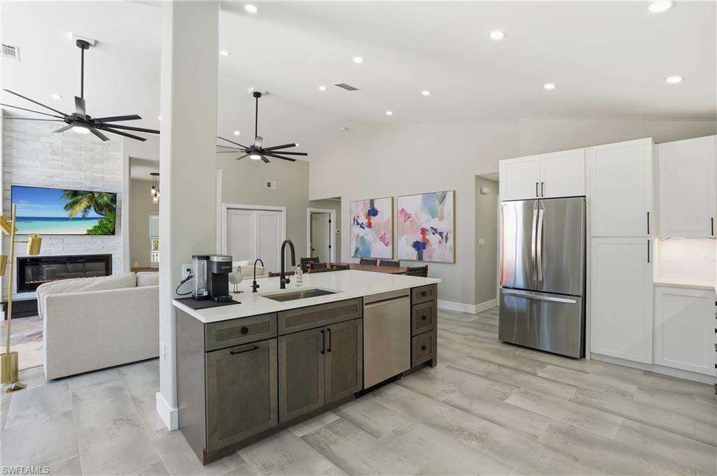 Kitchen with a fireplace, stainless steel appliances, open floor plan, two tone cabinetry, and recessed lighting - Virtually Edited Image