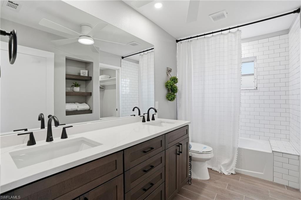 Bathroom featuring double vanity, ceiling fan, wood tiled floors, shower / bathtub combination with curtain, and recessed lighting - Virtually Edited Image