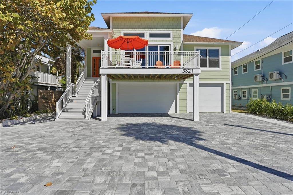 Raised beach house featuring an attached garage, decorative driveway, and a balcony - Virtually Edited Image