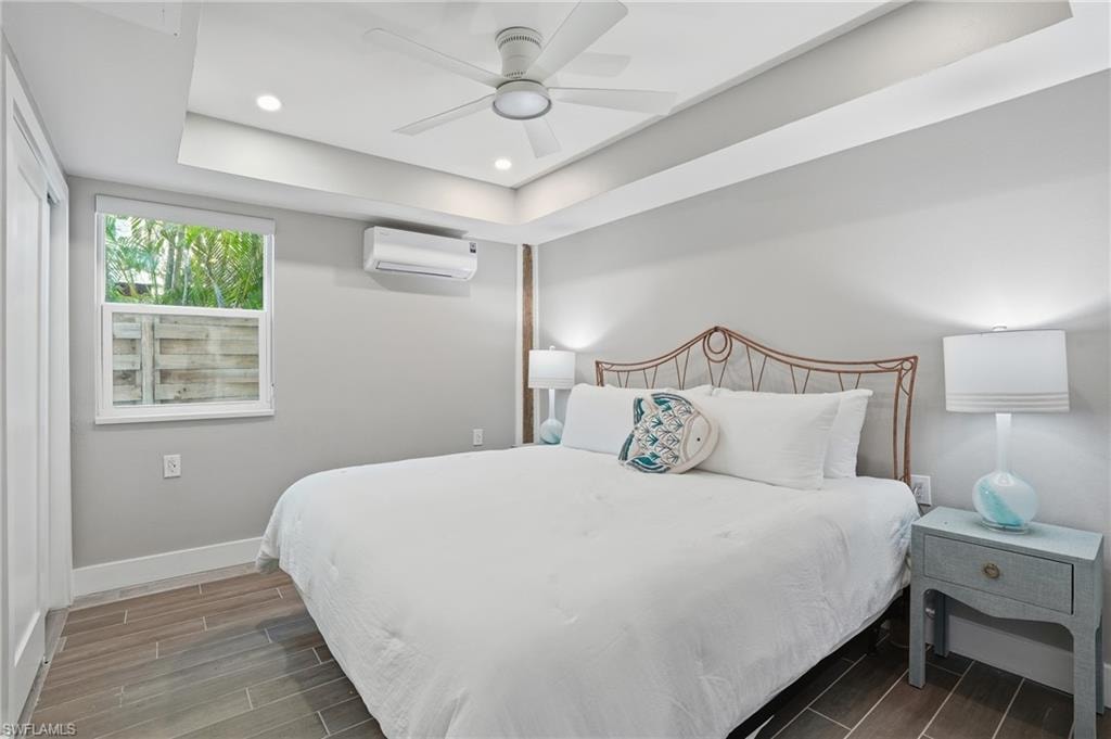 Bedroom with wood finish floors, a raised ceiling, recessed lighting, and ceiling fan - Virtually Edited Image