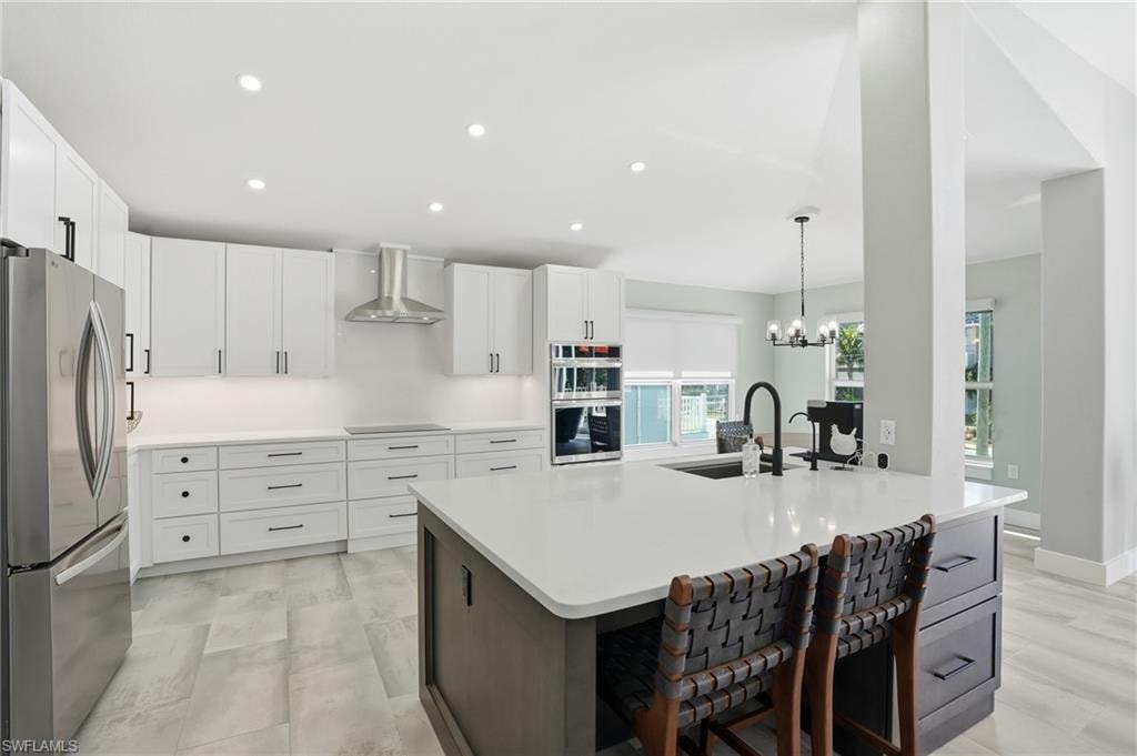 Kitchen with stainless steel appliances, a kitchen island with sink, suspended lighting, dual tone cabinetry, and light stone counters - Virtually Edited Image