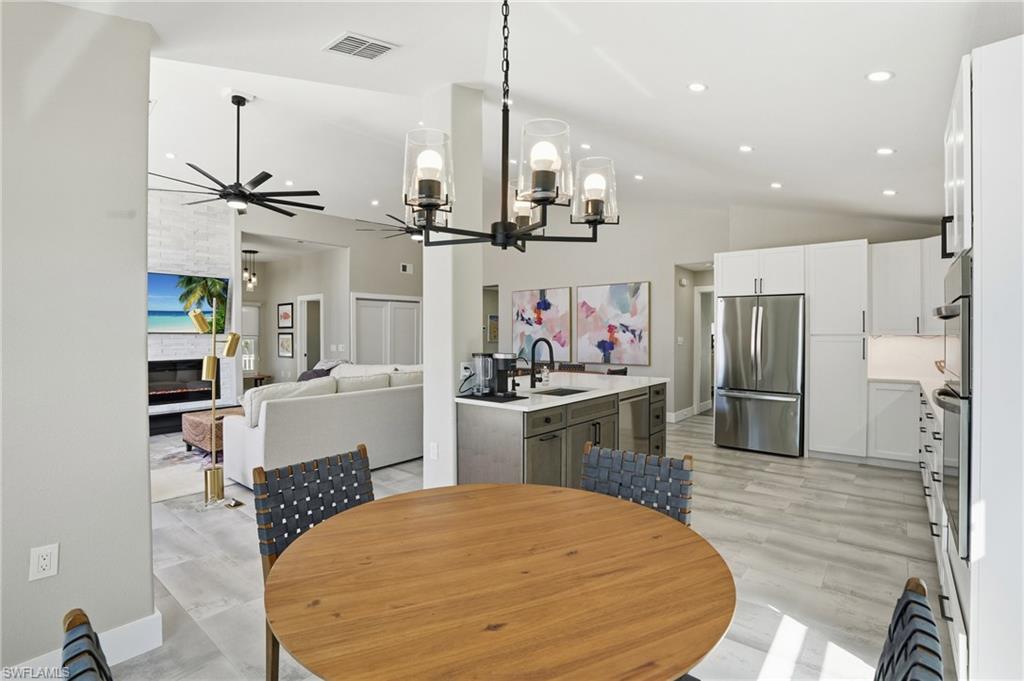 Dining area featuring hanging lights, a ceiling fan, a fireplace, light wood-style floors, and lofted ceiling - Virtually Edited Image