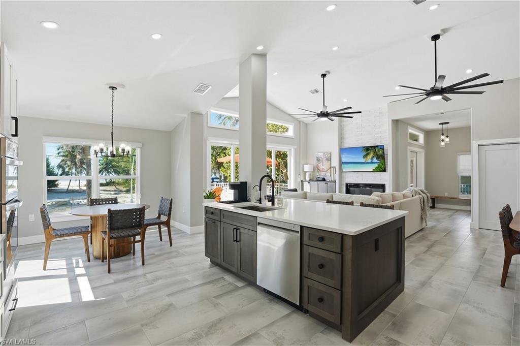 Kitchen featuring a chandelier, stainless steel appliances, vaulted ceiling, a fireplace, and open floor plan - Virtually Edited Image