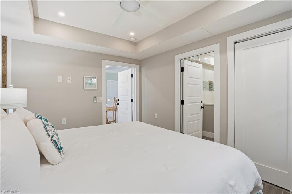 Bedroom with a raised ceiling, a ceiling fan, recessed lighting, and wood finished floors - Virtually Edited Image
