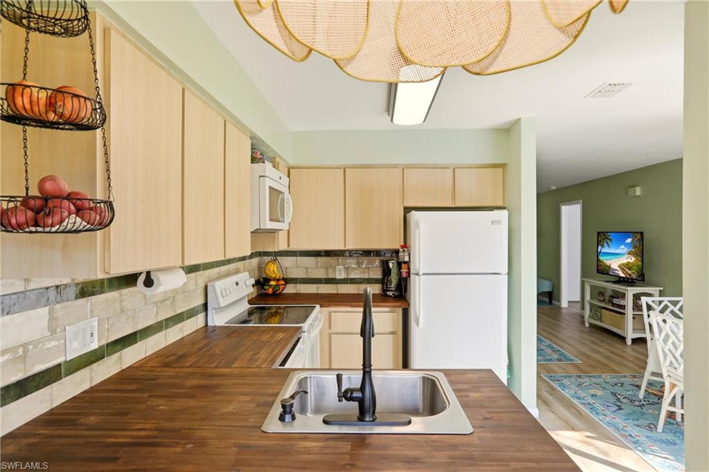 Kitchen with light wood finish cabinets, white appliances, backsplash, and wood finished floors