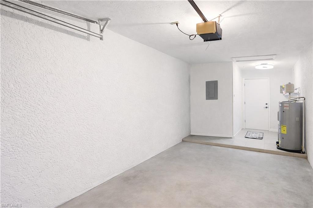 Garage featuring a textured wall, water heater, a garage door opener, and electric panel