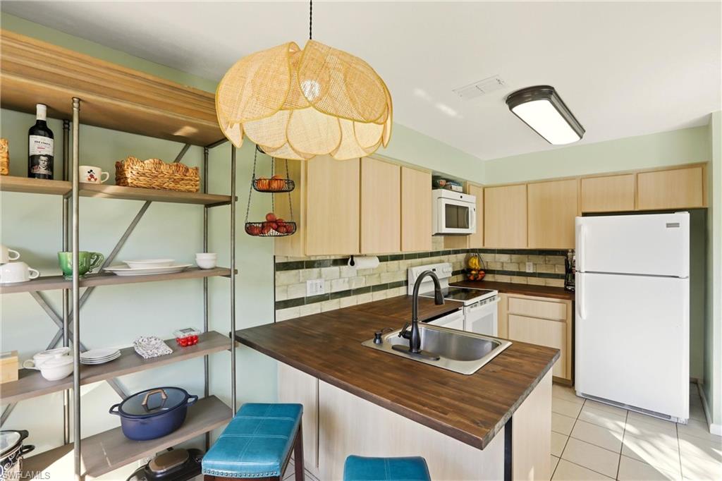 Kitchen featuring light wood finish cabinets, a peninsula, white appliances, and dark countertops