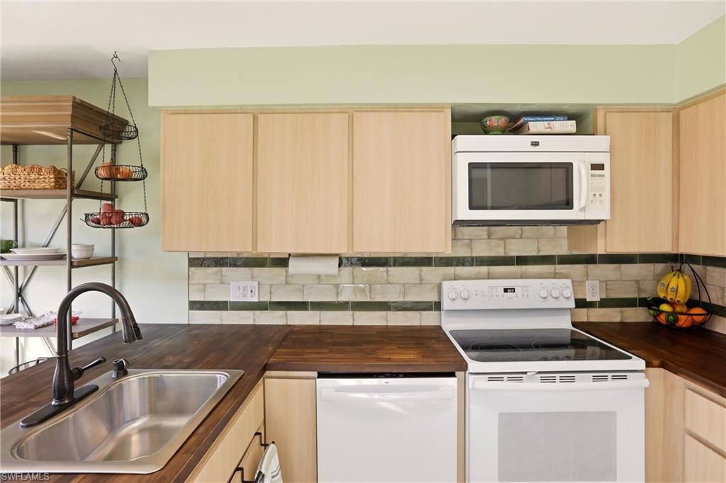 Kitchen featuring light wood finish cabinetry, white appliances, decorative backsplash, and butcher block countertops