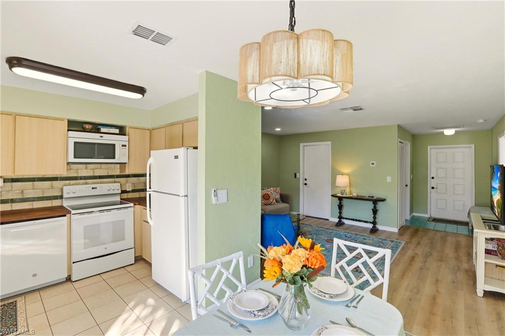 Kitchen with white appliances, light wood finish cabinets, tasteful backsplash, decorative light fixtures, and open floor plan