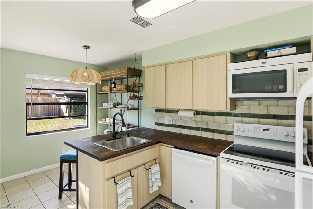 Kitchen featuring light wood finish cabinetry, white appliances, a peninsula, a breakfast bar, and pendant lighting