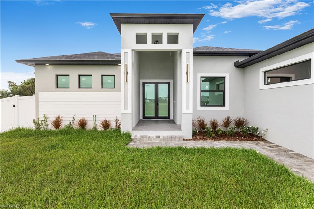 Property entrance featuring french doors, a lawn, stucco siding, and a shingled roof